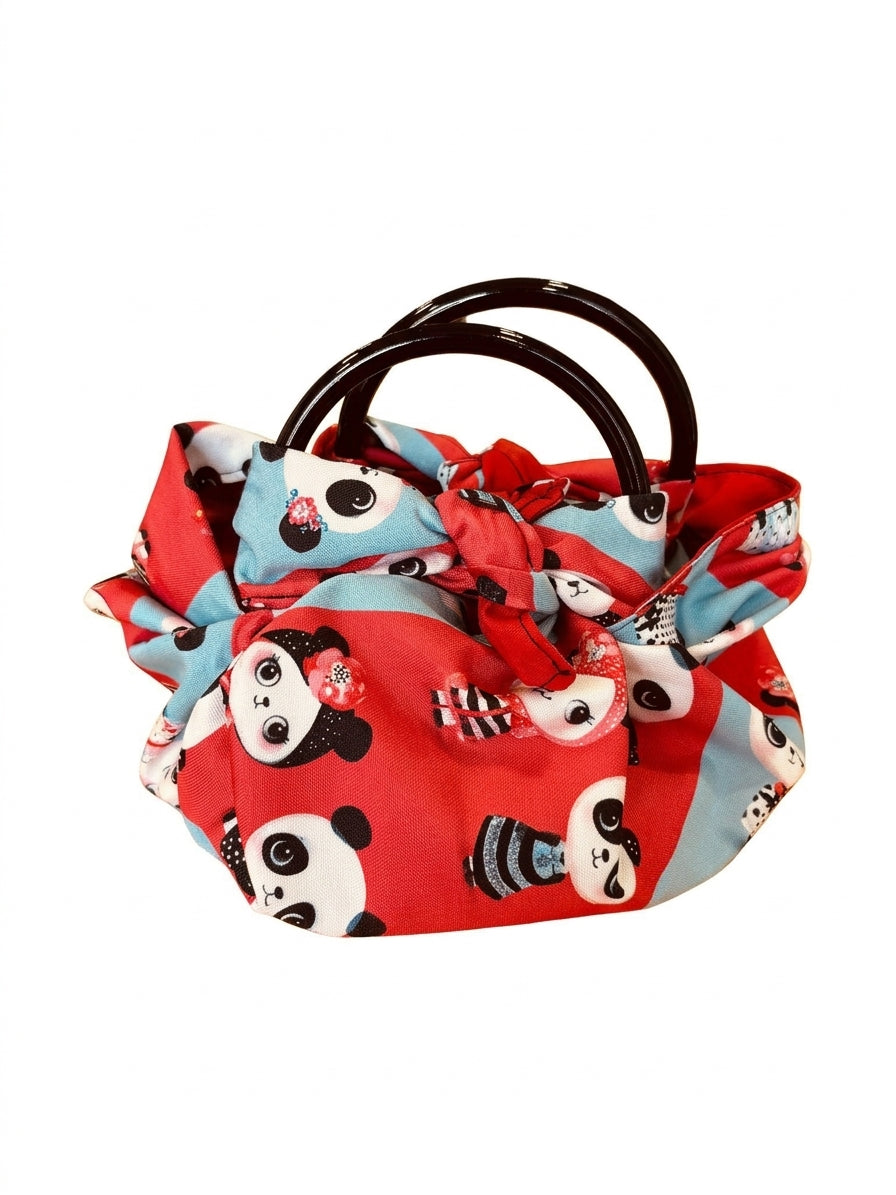 Handtasche „Panda“ aus rot-hellblauem Stoff mit niedlichem Panda-Muster, roten Stoffschleifen und dunkelbraunen runden Henkeln vor weißem Hintergrund.