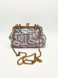 Bügeltasche LOVE LETTER in Grau und Rosa mit Schriftmuster, antikgoldfarbenem Bügelverschluss und langer goldfarbener Kette vor hellem Hintergrund.
