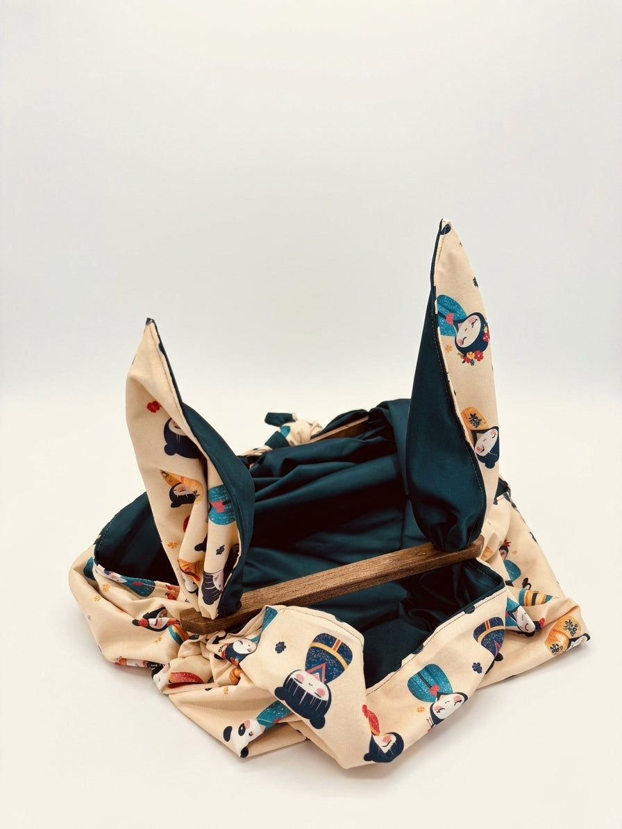 Innenansicht der Beuteltasche „Figuren“ mit dunkelblauem Innenfutter, cremefarbenem Stoff mit buntem Figurenmuster und Holzstäbchen zum Formen der Tasche.